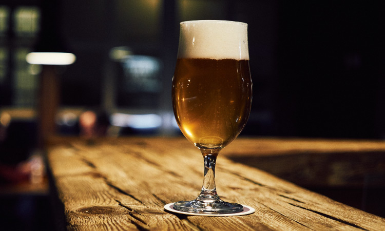 Closeup of a glass of alcoholic beer on a wooden counter at a bar that will increase your risk for cancer