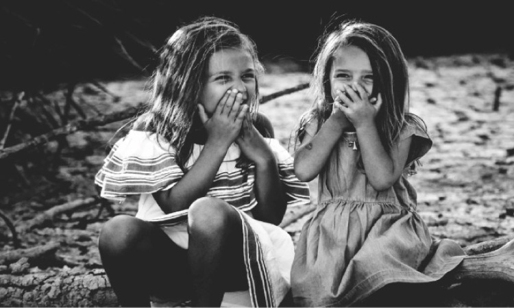 two young girls holding their mouths laughing