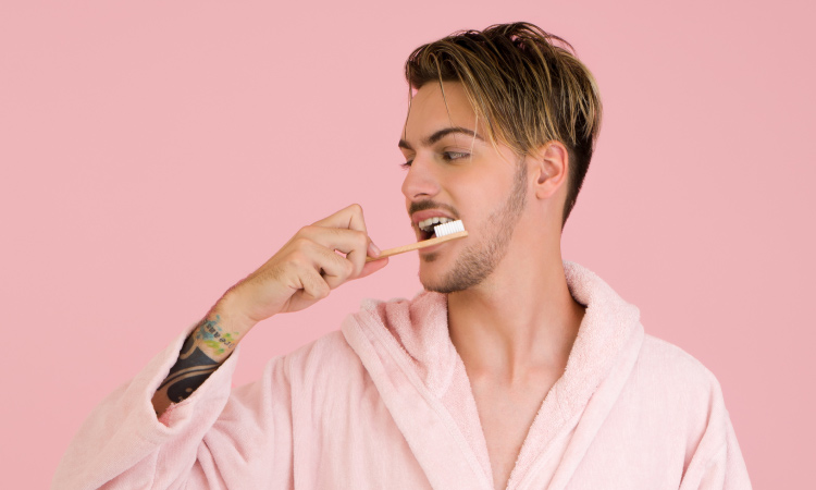 man wearing a bathrobe brushing his teeth to prevent tooth decay