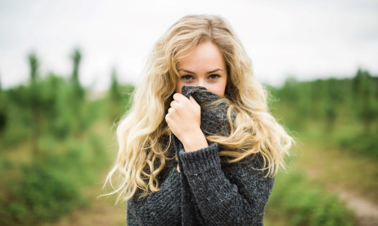 blonde woman hiding her mouth with her sweater neck