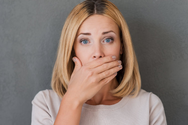 blond woman covering her mouth with her hand to hide swollen gums