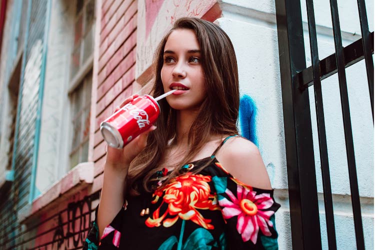 brown haired girl drinking a can of soda with straw