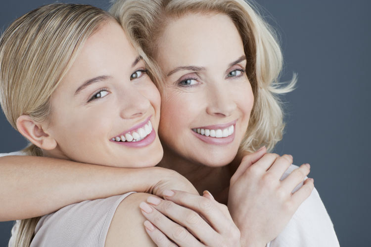 two blond women hug and smile to show off their white teeth