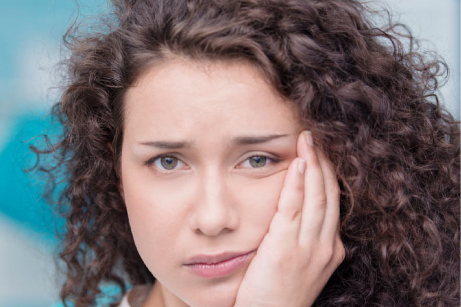 young woman holding her jaw in pain with emerging wisdom teeth