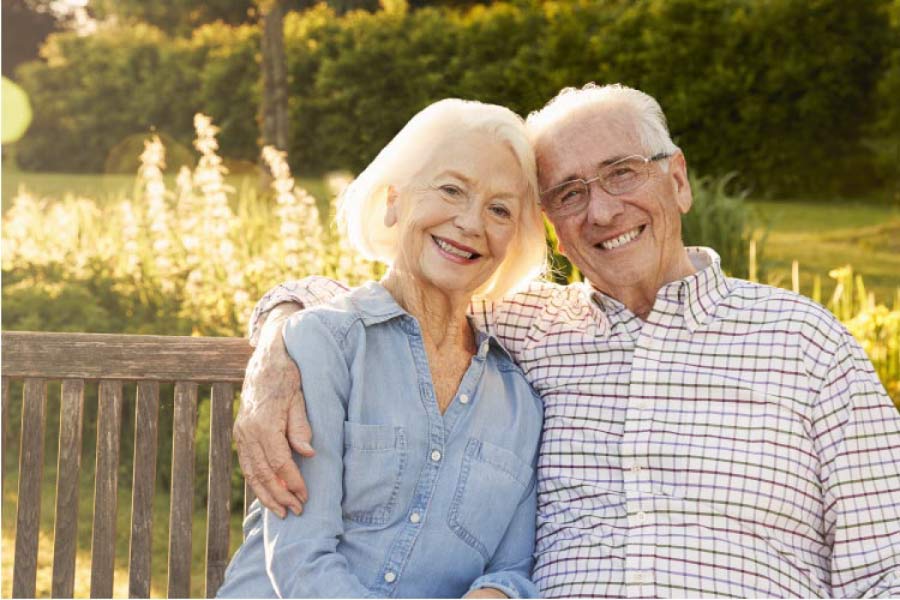 senior couple sitting on a bench hug and smile after learning about the health benefits of dentures