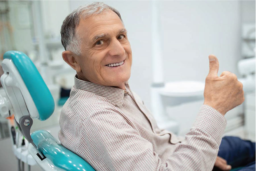 senior man in the dentist chair gives a thumbs up after a successful tooth replacement procedure